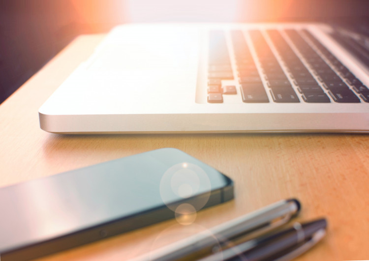 Ujęcie na klawiaturę komputera, telefon i długopisy leżące na biurku